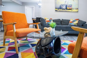 Ein modernes Wohnzimmer mit einem lebendigen geometrischen Teppich, einer Couch, einem Sessel und einem Couchtisch mit einer Pflanze.
