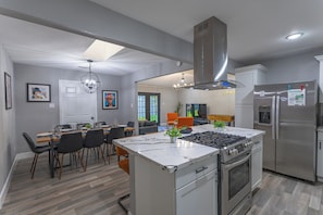 A modern kitchen with a central island, stainless steel appliances, and a dining area with chairs and a table. - Group Stay 4 Kanye | Reliant Stadium | Hot Tub | Cinema (Houston)