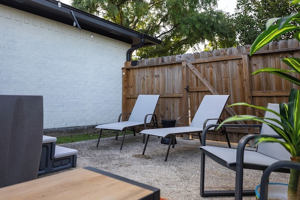 Ein Terrassenbereich im Freien mit einer weißen Ziegelwand, einem Holzzaun und drei weißen Lounge-Stühlen.