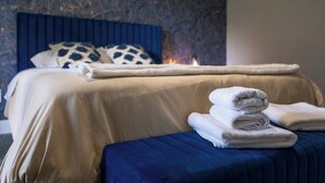 A neatly made bed with a blue headboard, a bedside table with folded white towels, and a lit candle on the bed. - Outdoor Cinema | Hot Tub | Fire Pit | Huge Yard (Houston)