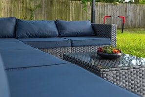 Un canapé modulable avec des coussins, une table basse en verre au motif tissé et une plante en pot aux fleurs colorées.