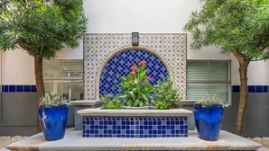 Un espace extérieur carrelé, agrémenté d’un jardin central, de deux grands pots de fleurs et d’un mur décoratif.