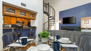 Une cuisine moderne avec des meubles en bois, un escalier en colimaçon, un téléviseur à écran plat et un coin repas avec une table en verre, mise pour deux personnes.