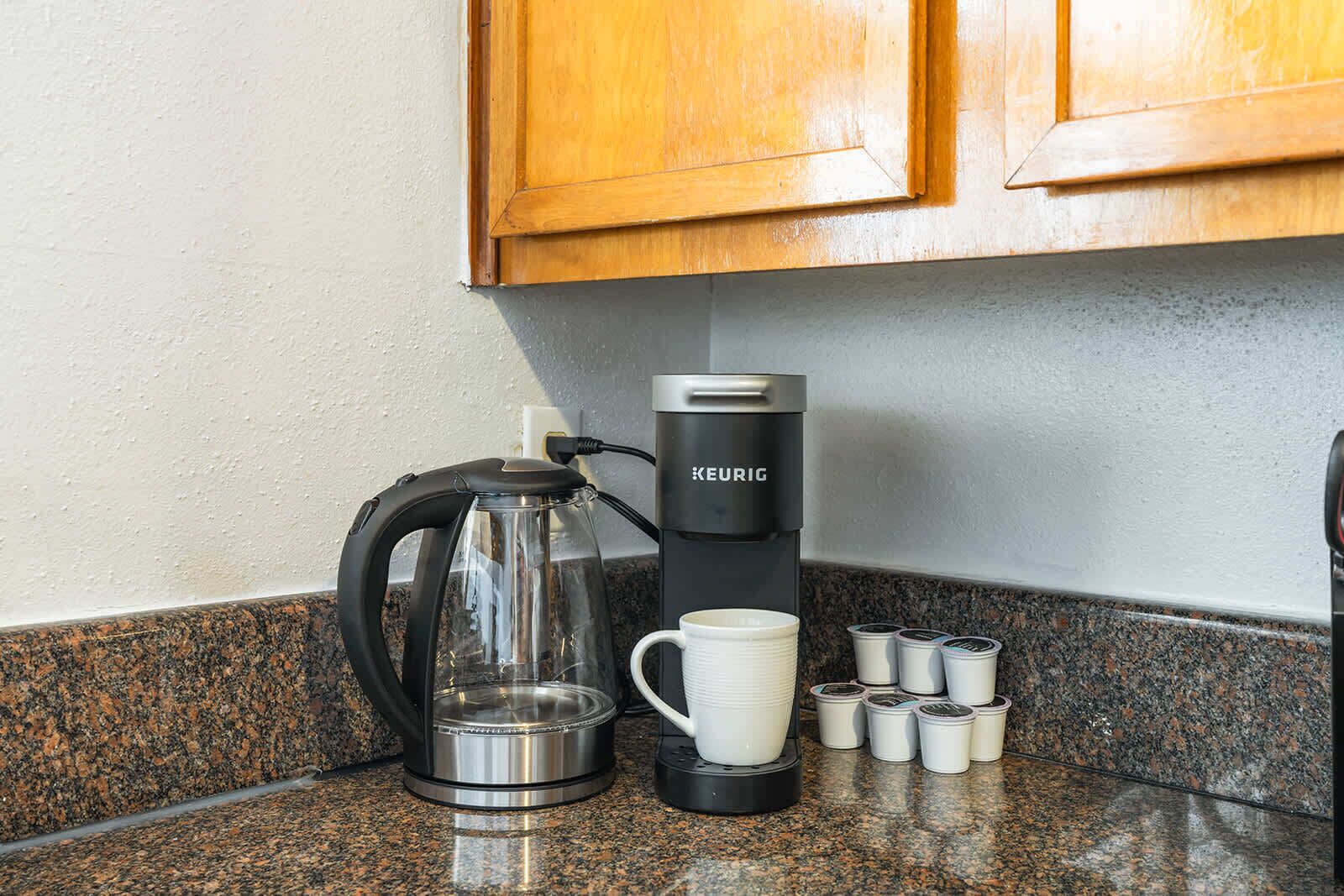 Una cafetera, una jarra de vidrio y varias tazas de café sobre una encimera de granito.