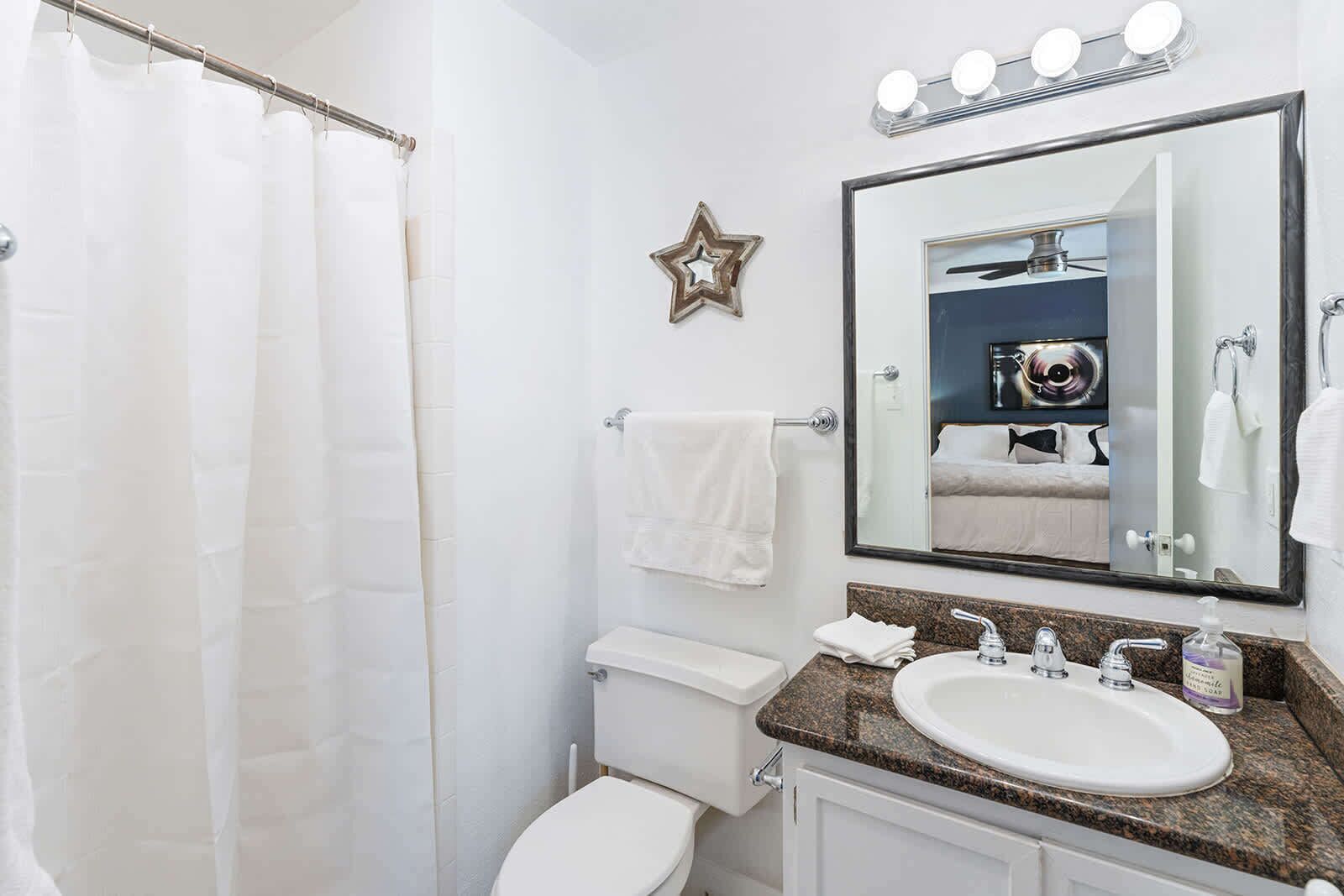Une salle de bain avec un rideau de douche, des toilettes, un lavabo avec un miroir et une décoration en forme d’étoile sur le mur.