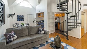 Un salon moderne avec un canapé gris, un escalier en colimaçon et une cuisine en arrière-plan.