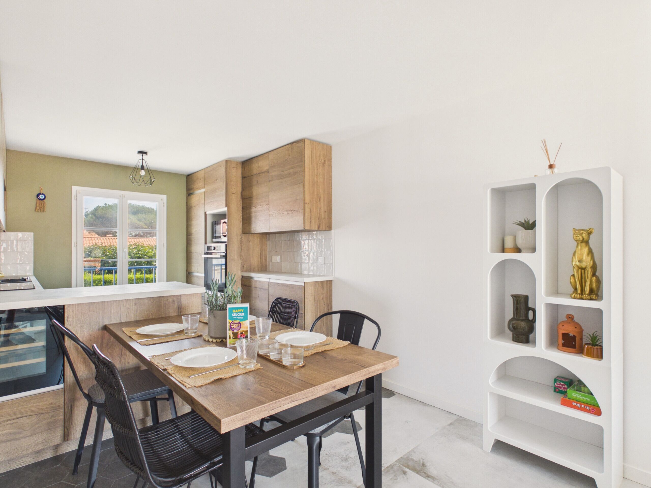 A modern kitchen with wooden cabinets, a dining table set for four, and a white shelving unit with decorative items.