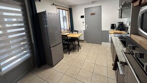 A compact kitchen with a refrigerator, stove, microwave, and a dining area with a table and chairs. - Gîte du Tacot 21 – A peaceful retreat in the heart of nature (Saulieu)