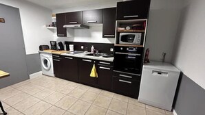 A compact kitchen with a washing machine, microwave, and a small refrigerator. - Gîte du Tacot 21 – A peaceful retreat in the heart of nature (Saulieu)