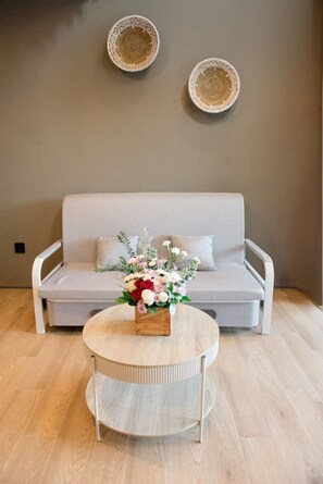 A modern living room with a grey sofa, a round coffee table with a floral centerpiece, and two woven wall decorations. - Cozy Mezzanine Loft Bedroom and Master Suite with Shared Pool & Co-Work Deck (badung)