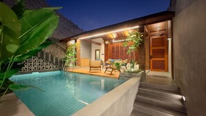 A swimming pool with a wooden deck, a seating area with chairs, and a staircase leading to a door.