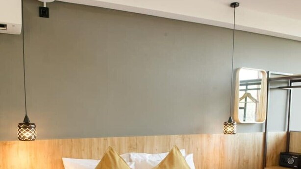 A hotel room with a bed, wooden headboard, bedside tables, a mirror, and a radio.