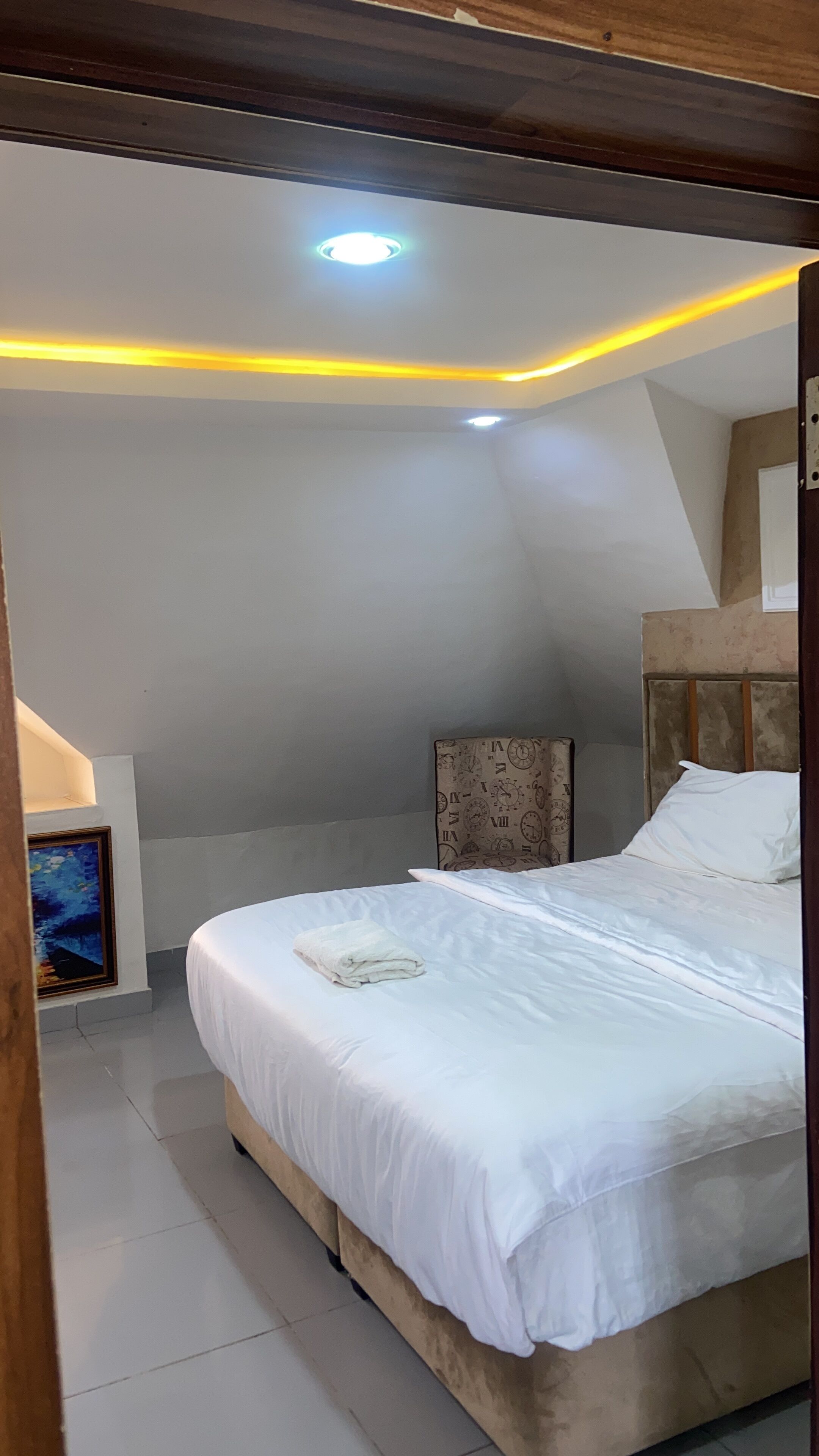 A bedroom with a bed, a nightstand, a wall clock, and a ceiling light.
