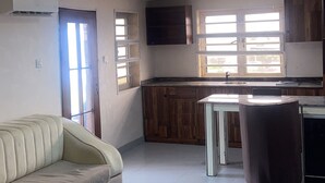 A living room with a sofa, a colorful rug, a kitchen area with wooden cabinets, and a dining table. - Wimpy hotel and suite beachfront (Lekki)