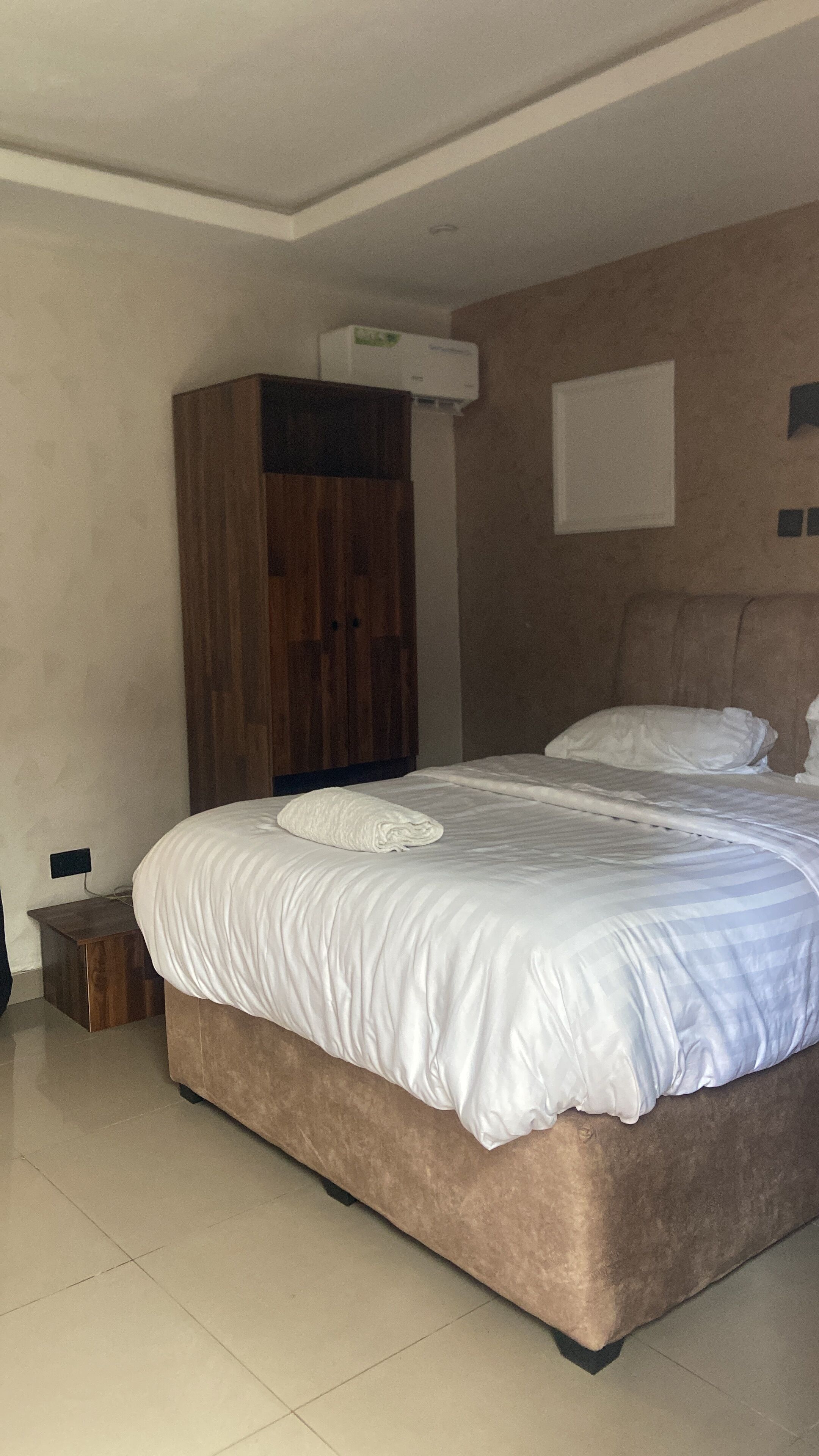 Un dormitorio con una cama grande, un armario de madera, un equipo de aire acondicionado y una mesita de noche pequeña.
