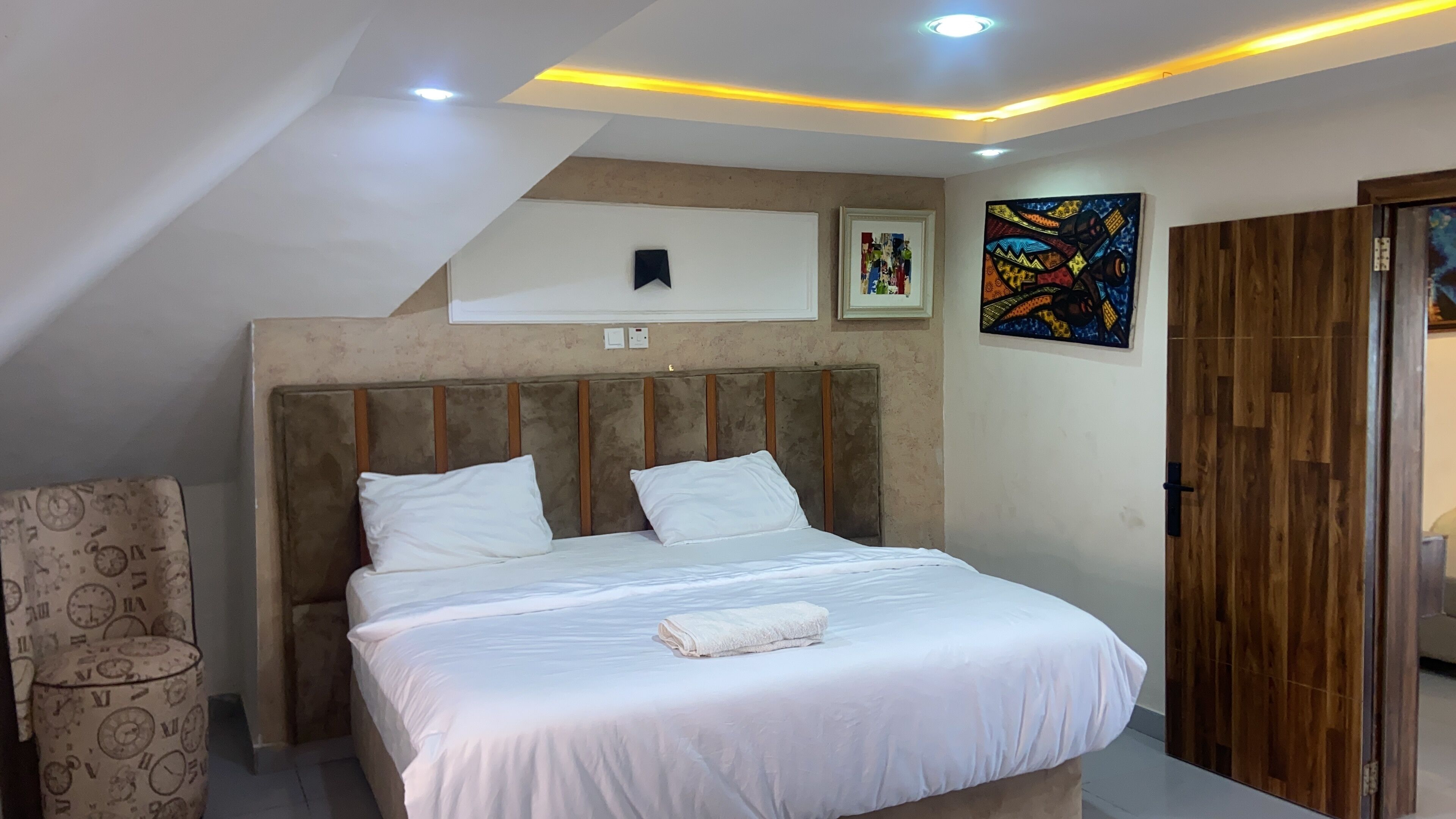 A bedroom with a bed, a headboard, a wall-mounted artwork, and a wooden wardrobe.