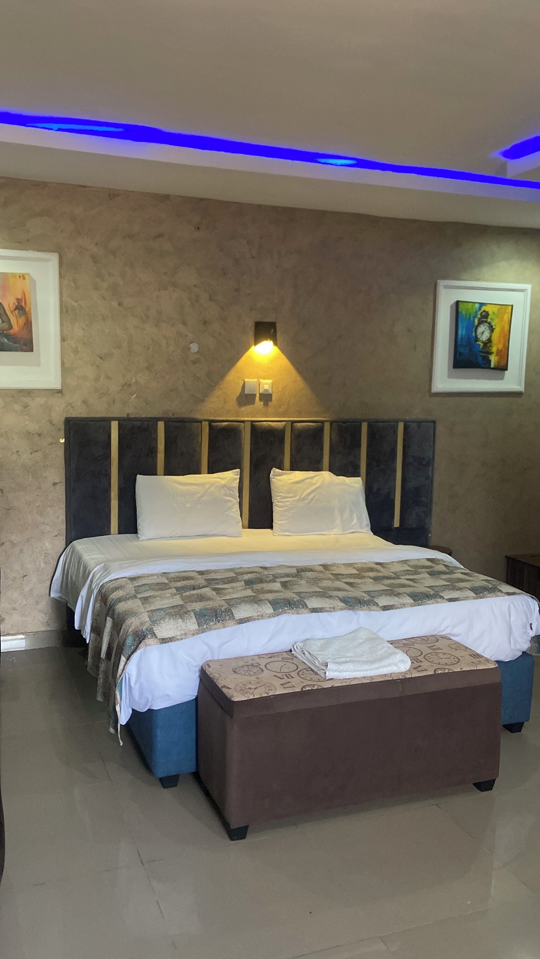 Un dormitorio con una cama, una mesita de noche, una lámpara de pared y dos cuadros enmarcados.