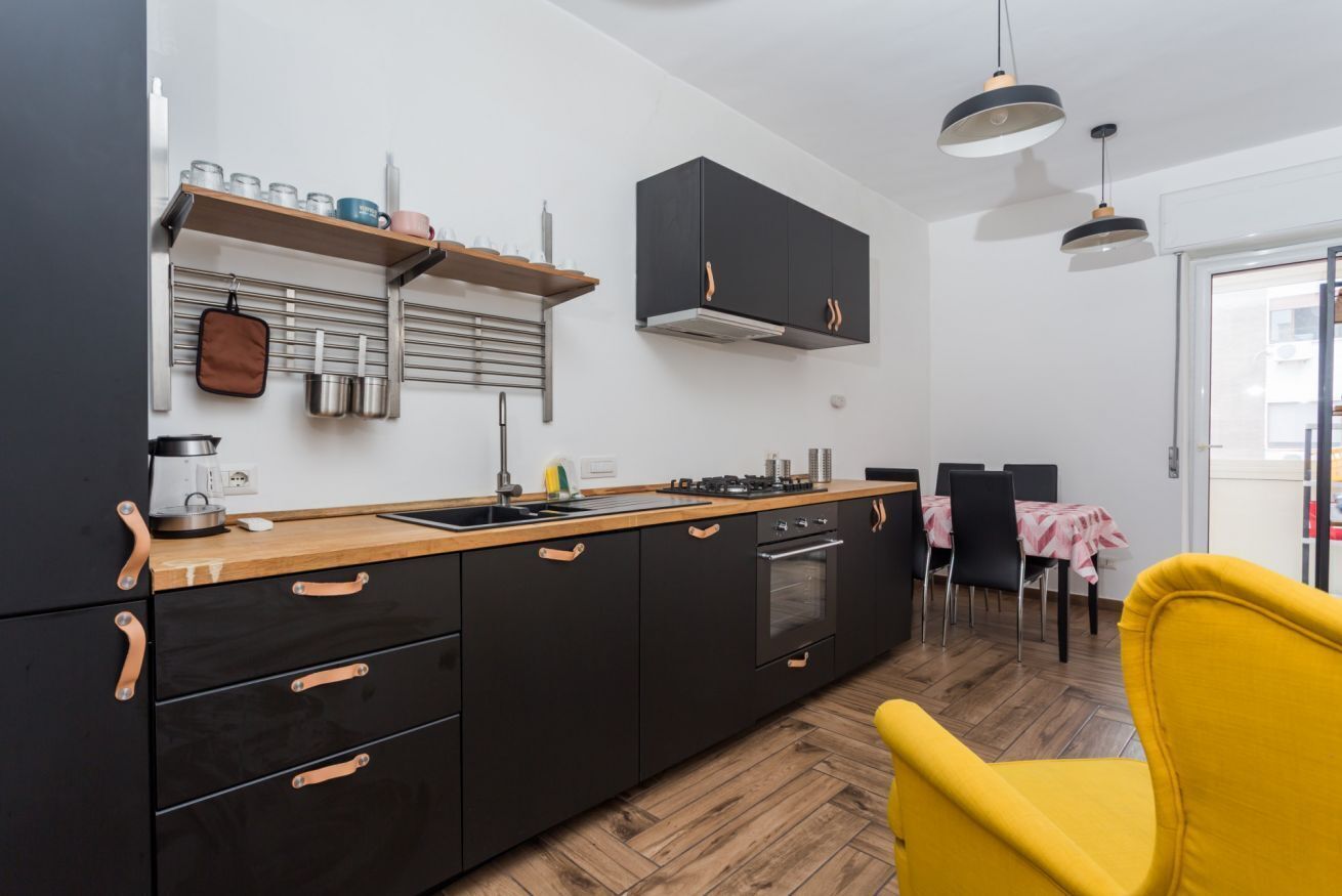 Una cucina moderna con mobili neri, piano di lavoro in legno e una sedia gialla.