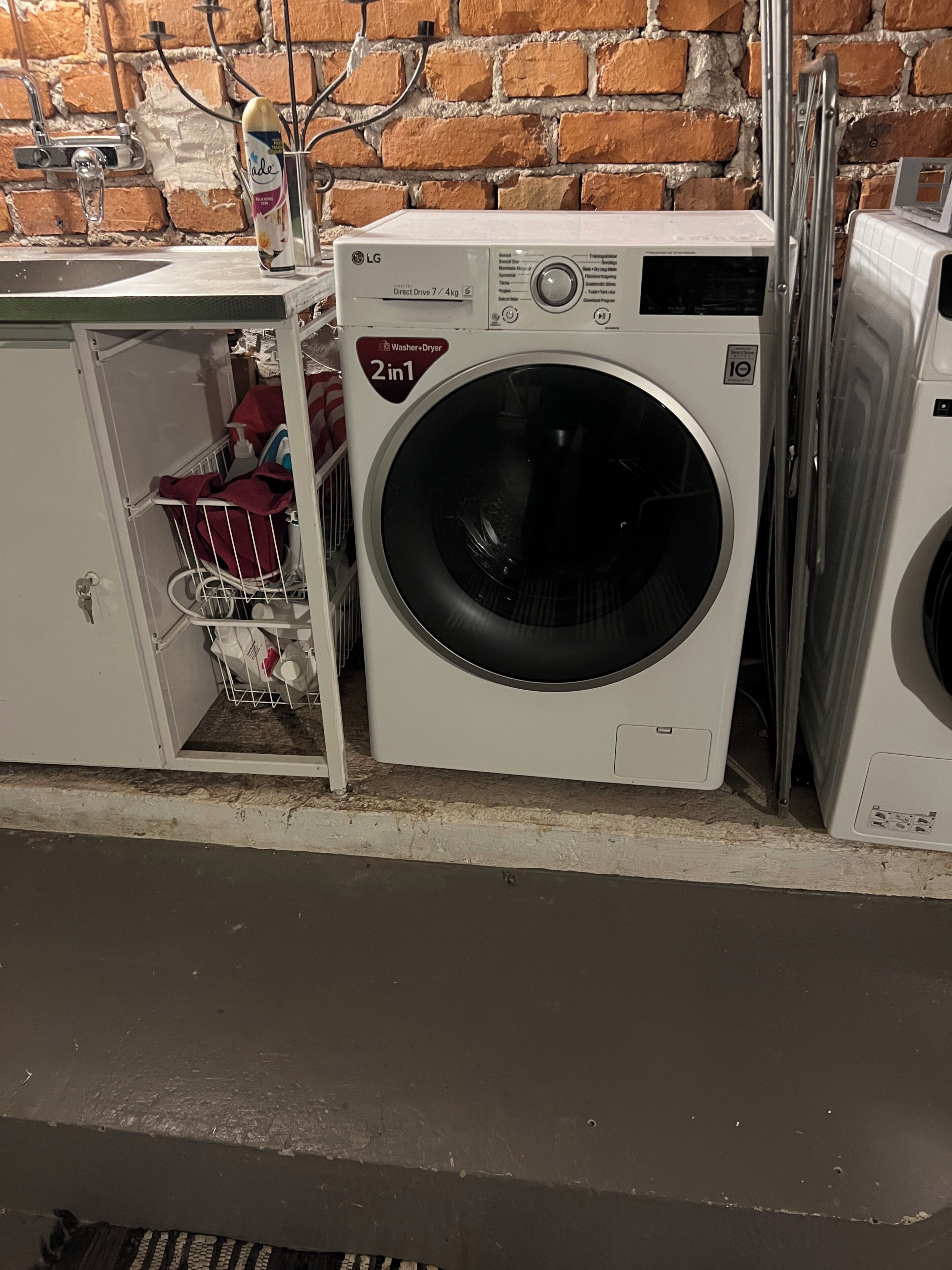 A compact washer-dryer unit with a 2-in-1 function, placed in a utility room with a brick wall background.