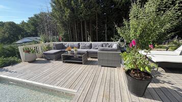 Eine Holzterrasse mit Gartenmöbeln, einem Swimmingpool und umgebender Bepflanzung.
