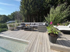 A wooden deck with outdoor furniture, a swimming pool, and surrounding greenery.