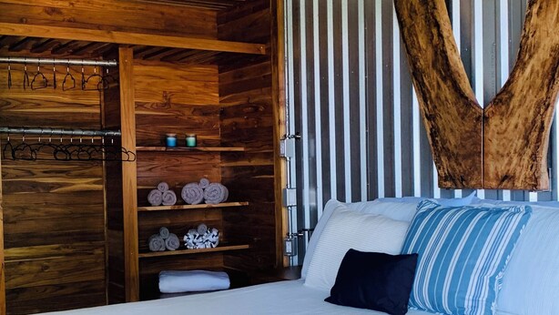 A bedroom with a wooden bed frame, a large wooden wardrobe, and a unique ceiling feature. - Uniquely Designed Casita with a Beautiful View (Nuevo Arenal)
