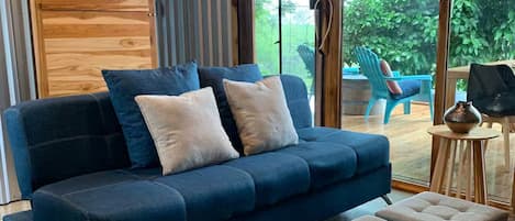 A modern living room with a blue sofa, two ottomans, and a wooden wall.