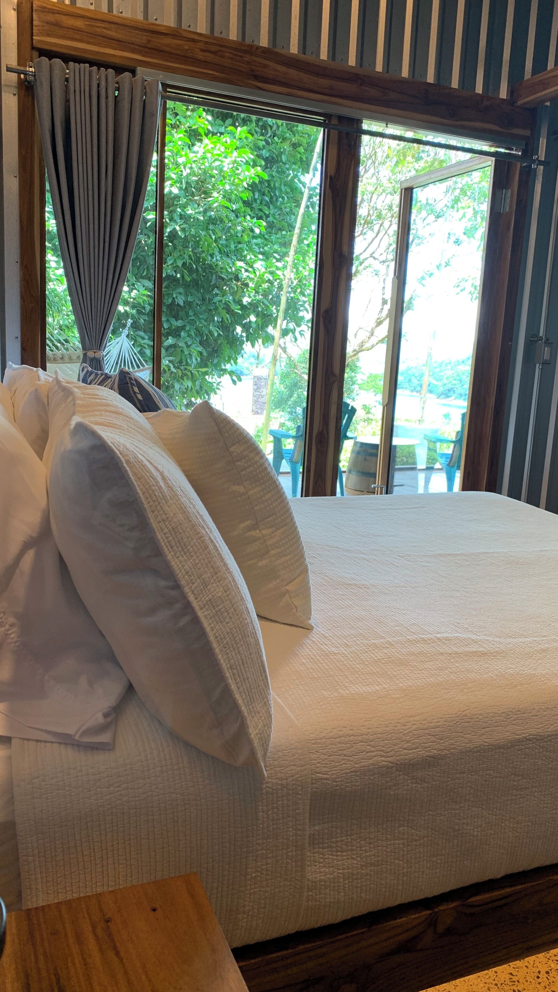 A bed with white bedding and a view of greenery outside.