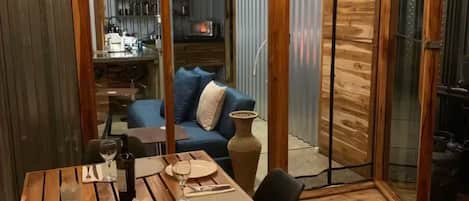 A dining area with a wooden table set for two, a kitchen in the background, and a sliding glass door leading to a living area.