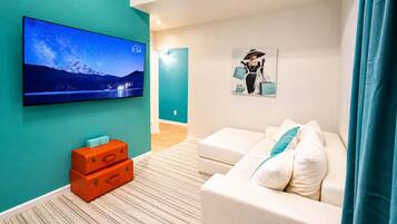 Un salon moderne avec un téléviseur à écran plat, un canapé, un tableau et une paire de valises orange.