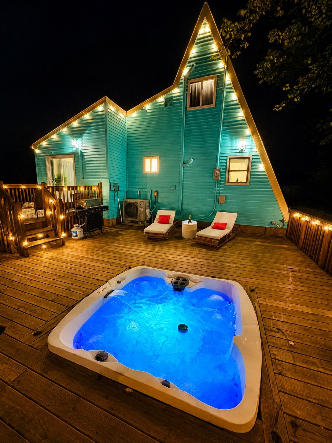 A house with a hot tub on a wooden deck, a barbecue grill, and two lounge chairs.