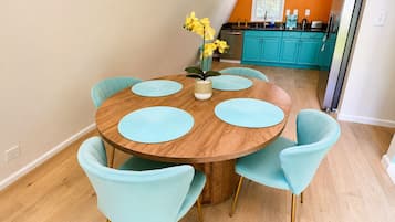Un comedor con una mesa redonda de madera, seis sillas azul claro y un jarrón con flores amarillas.