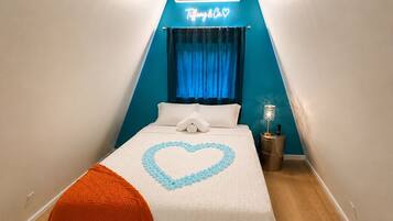 Une chambre avec un lit, un lustre, un néon et un rideau bleu.