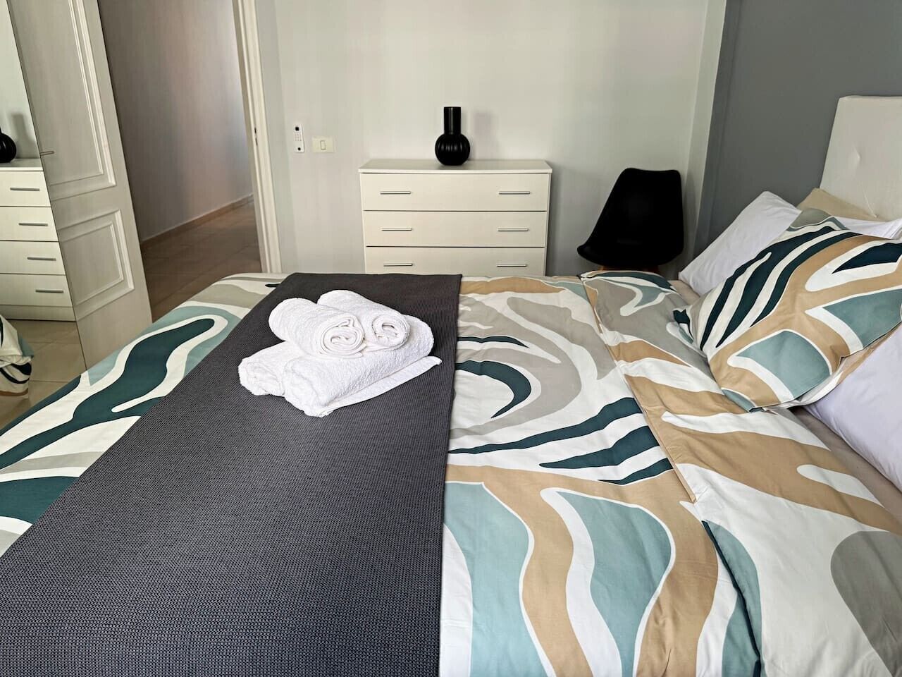 A hotel room with a bed, a bedside table, a lamp, and a wall-mounted vase.