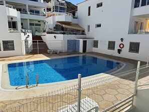 Ein Swimmingpool, umgeben von einem weißen Gebäude mit Balkonen und einer gefliesten Terrasse.