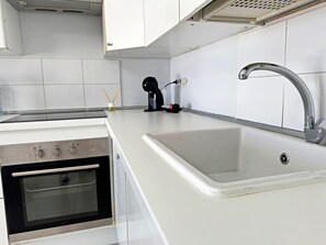 Eine Küche mit weißer Arbeitsplatte, einer Edelstahl-Spüle und einem eingebauten Backofen.
