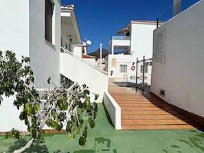 A rooftop terrace with a green floor, white walls, and a tree in the foreground. - Apartment in Los Cristianos - Ocean View (Arona)
