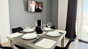 A dining area with a table set for four, a flat-screen TV mounted on the wall, and a window with curtains. - Apartment in Los Cristianos - Ocean View (Arona)