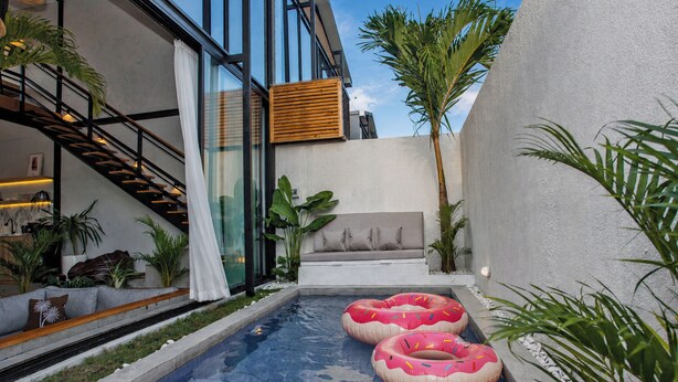 Un área de piscina exterior moderna con pared de vidrio, cubierta de madera y dos flotadores inflables.