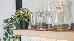 Una estantería con copas de vino, una jarra y una planta en maceta frente a una pared de mármol.