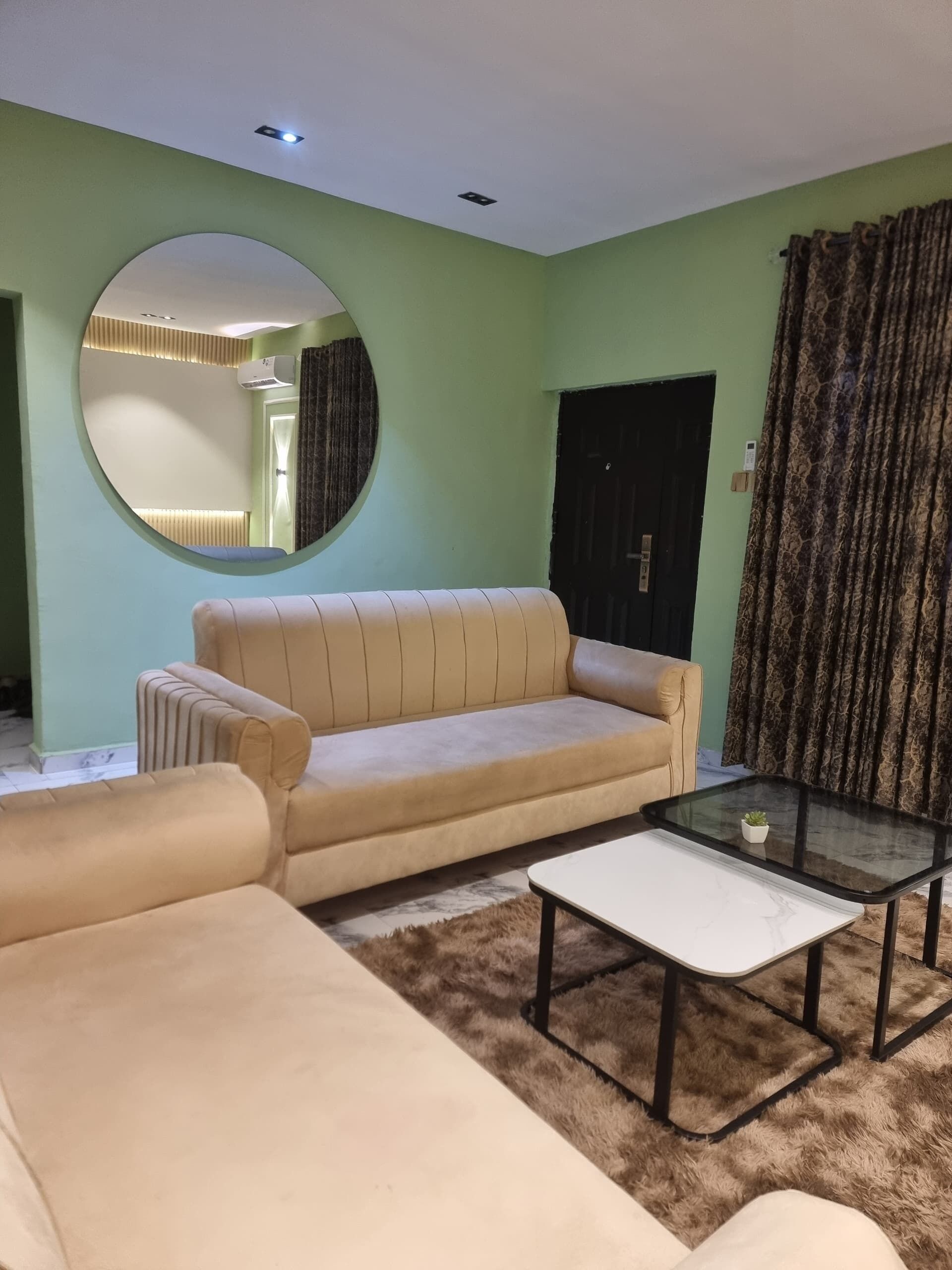 A living room with a sofa, a coffee table, a round mirror, and a door.