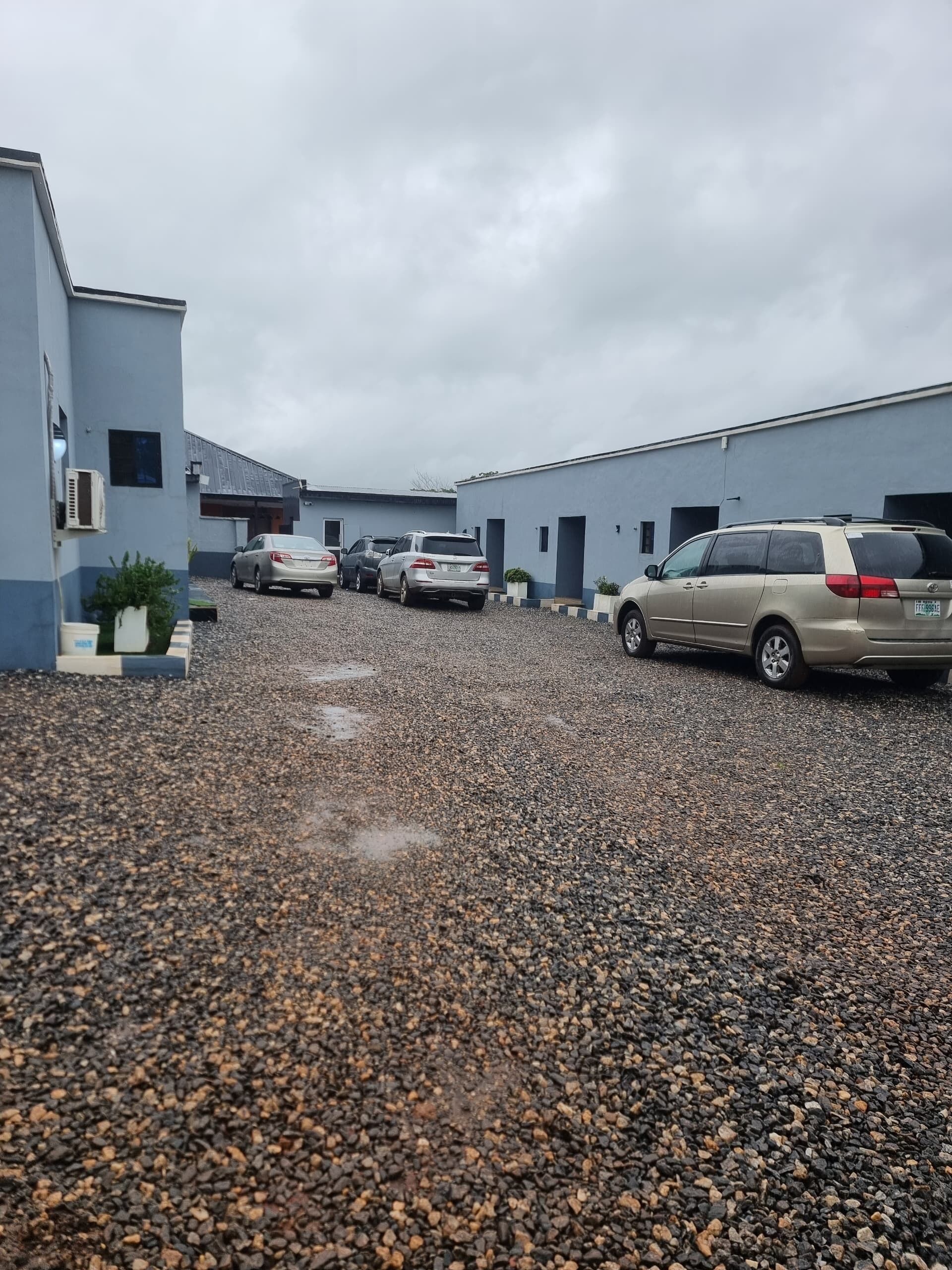 A parking area with multiple cars, gravel ground, and a building with a flat roof.