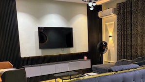 A modern living room with a flat-screen TV, a sofa, a dining table, and a patterned rug. - The Haven Hub (Abeokuta)