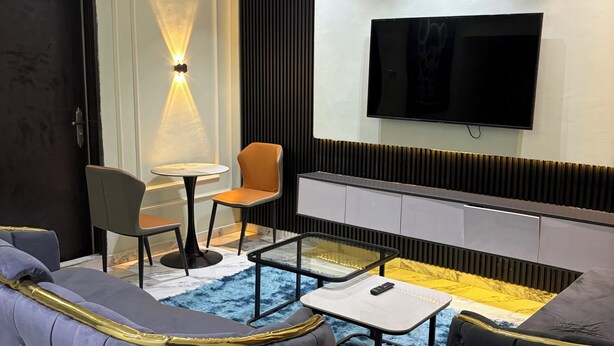 A modern living room with a sofa, a TV, a small table, and a chair. - The Haven Hub (Abeokuta)