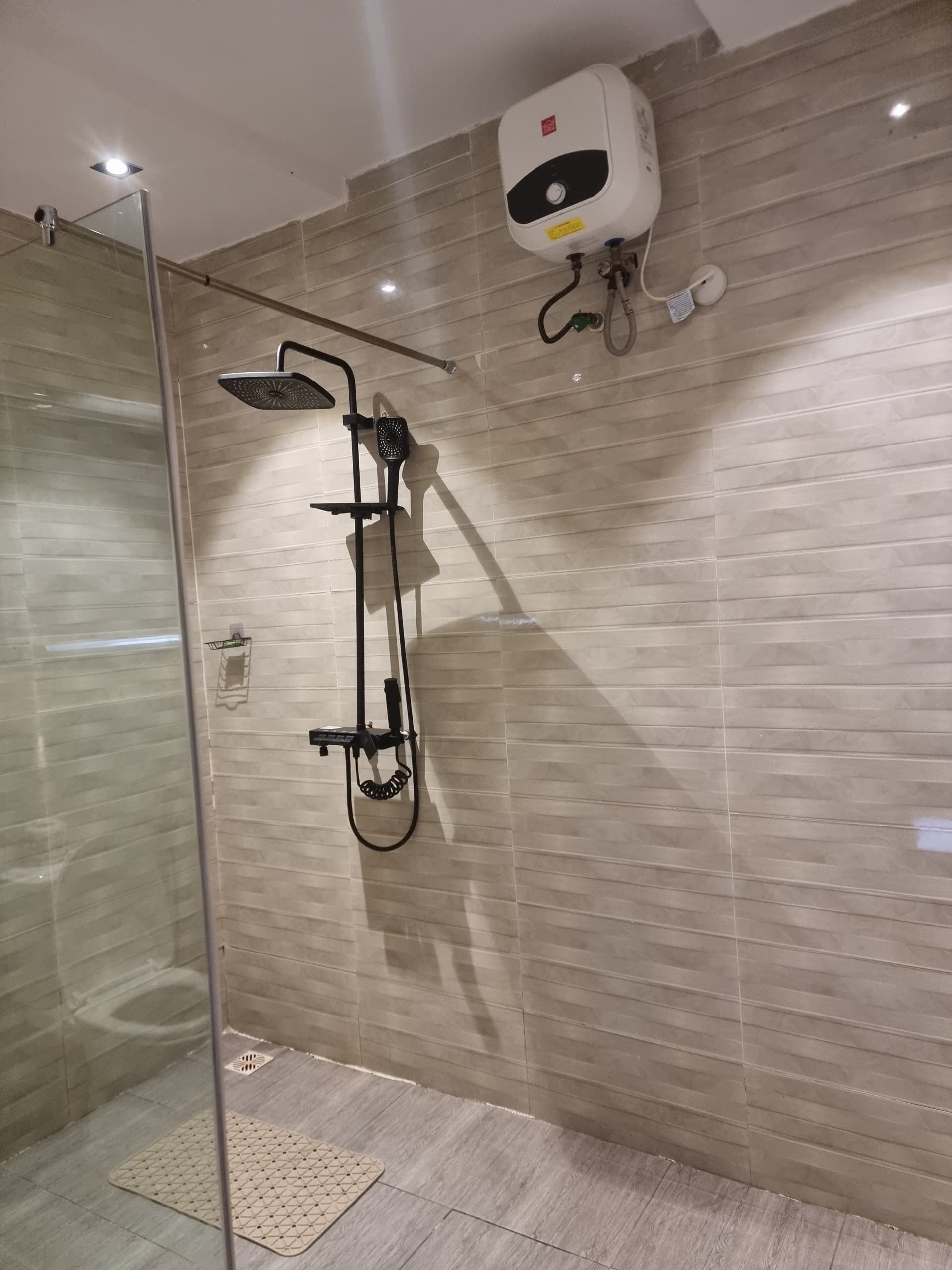 A modern bathroom with a glass-enclosed shower, a handheld showerhead, and a wall-mounted water heater.