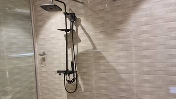 A modern bathroom with a glass-enclosed shower, a handheld showerhead, and a wall-mounted water heater.