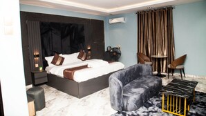 A modern bedroom with a large bed, a sofa, a small table, and a chair. - The Haven Hub (Abeokuta)