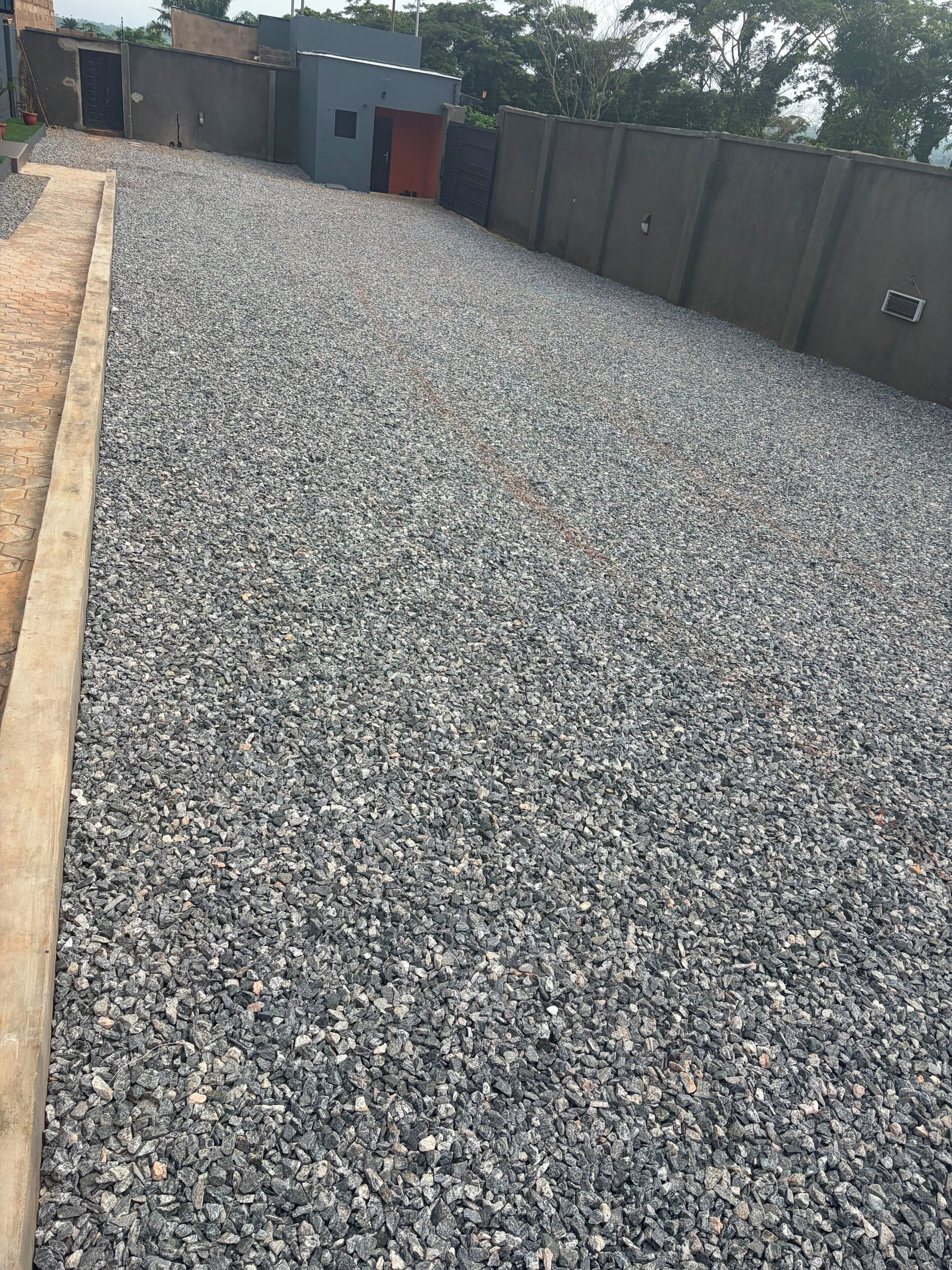 A gravel-covered rooftop with a low wall and a small building with a door.