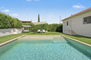A swimming pool with a clear blue water surface, surrounded by a well-maintained lawn and a white building with a tiled roof.