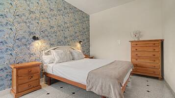Un dormitorio con una cama, mesitas de noche de madera, un aparador y una pared con estampado floral.